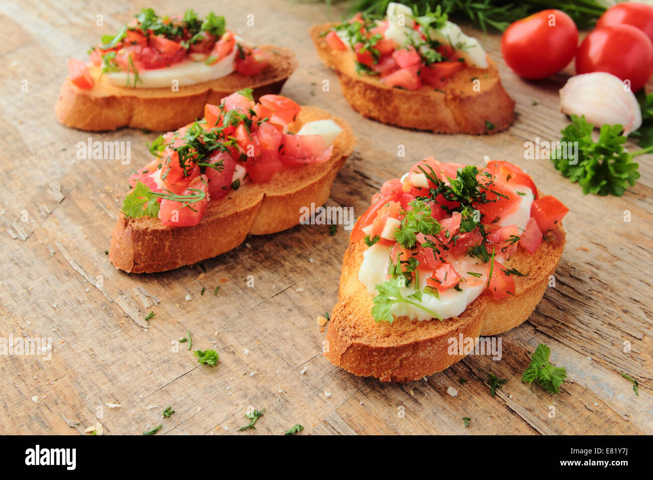 Antipasto fresco chiamato bruschetta con pomodoro, aglio, formaggio ed erbe su una tavola di legno Foto Stock