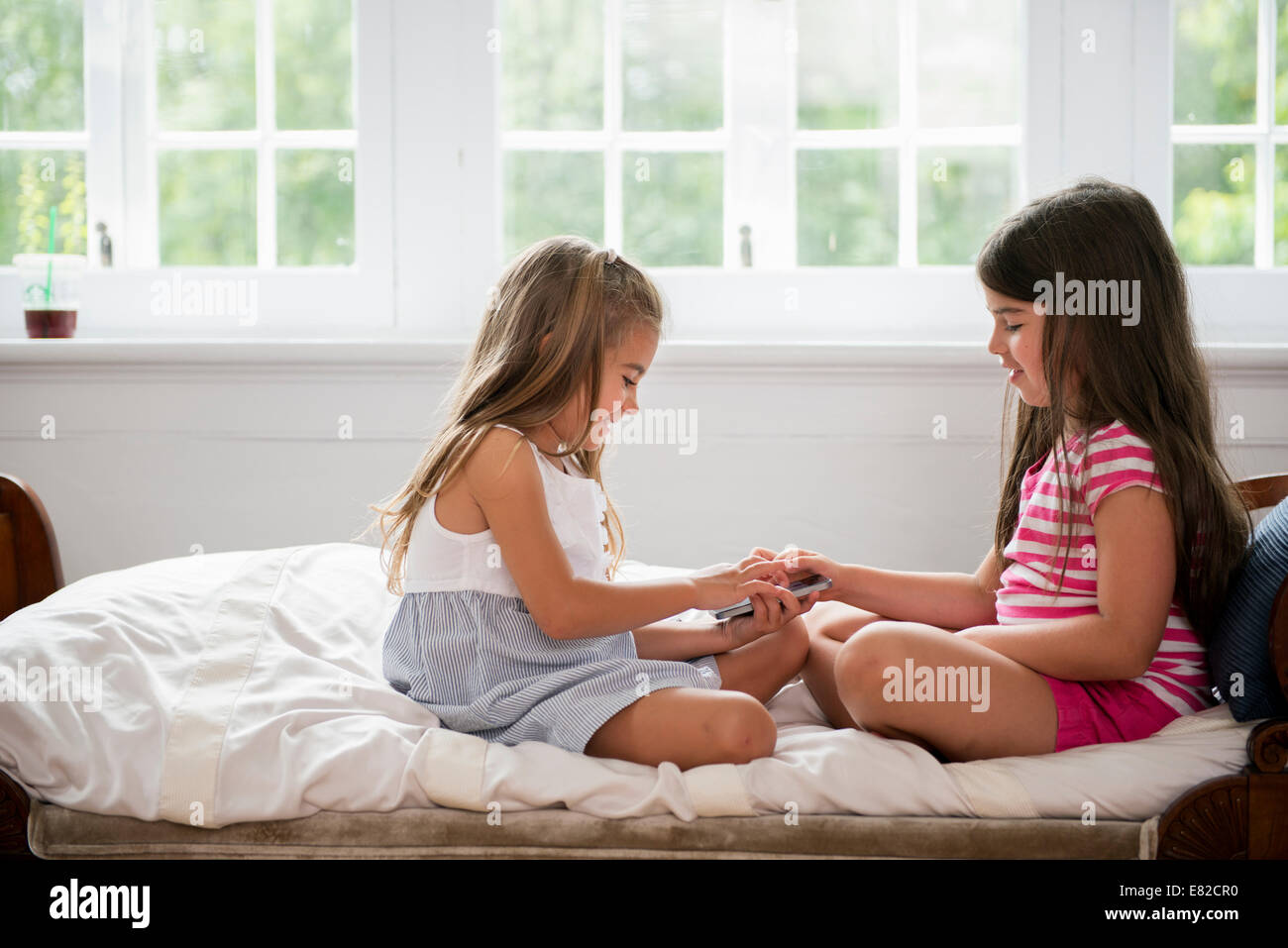 Due ragazze seduta diramazioni trasversali affacciate, tenendo in mano un telefono intelligente. Foto Stock