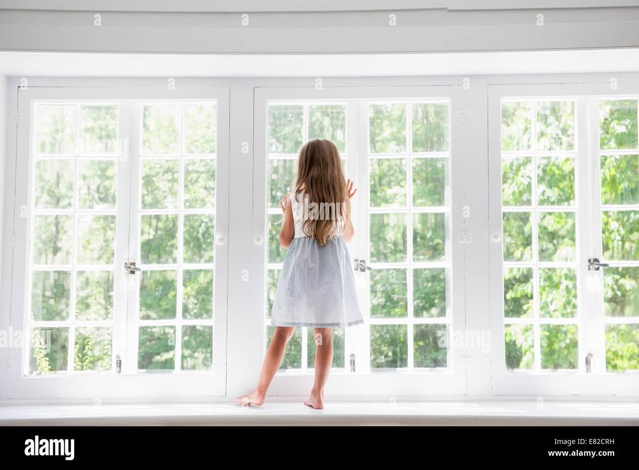 Un bambino in piedi in corrispondenza di una finestra che guarda fuori. Foto Stock