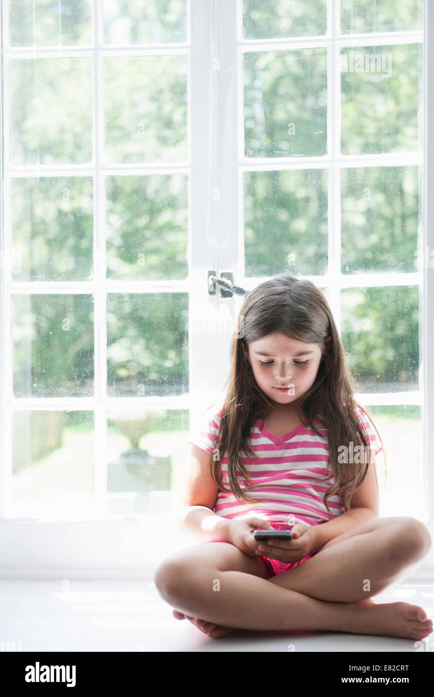 Una ragazza seduta giocando, tenendo in mano un telefono intelligente. Foto Stock