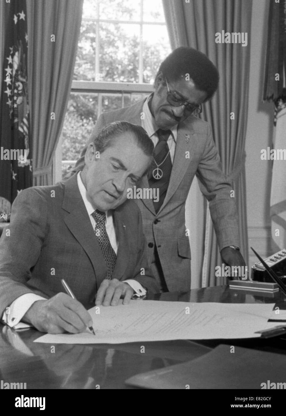 Il presidente Richard Nixon firma un documento alla sua scrivania in ufficio ovale come Sammy Davis Jr., guarda a. Luglio 1, 1971 Foto Stock