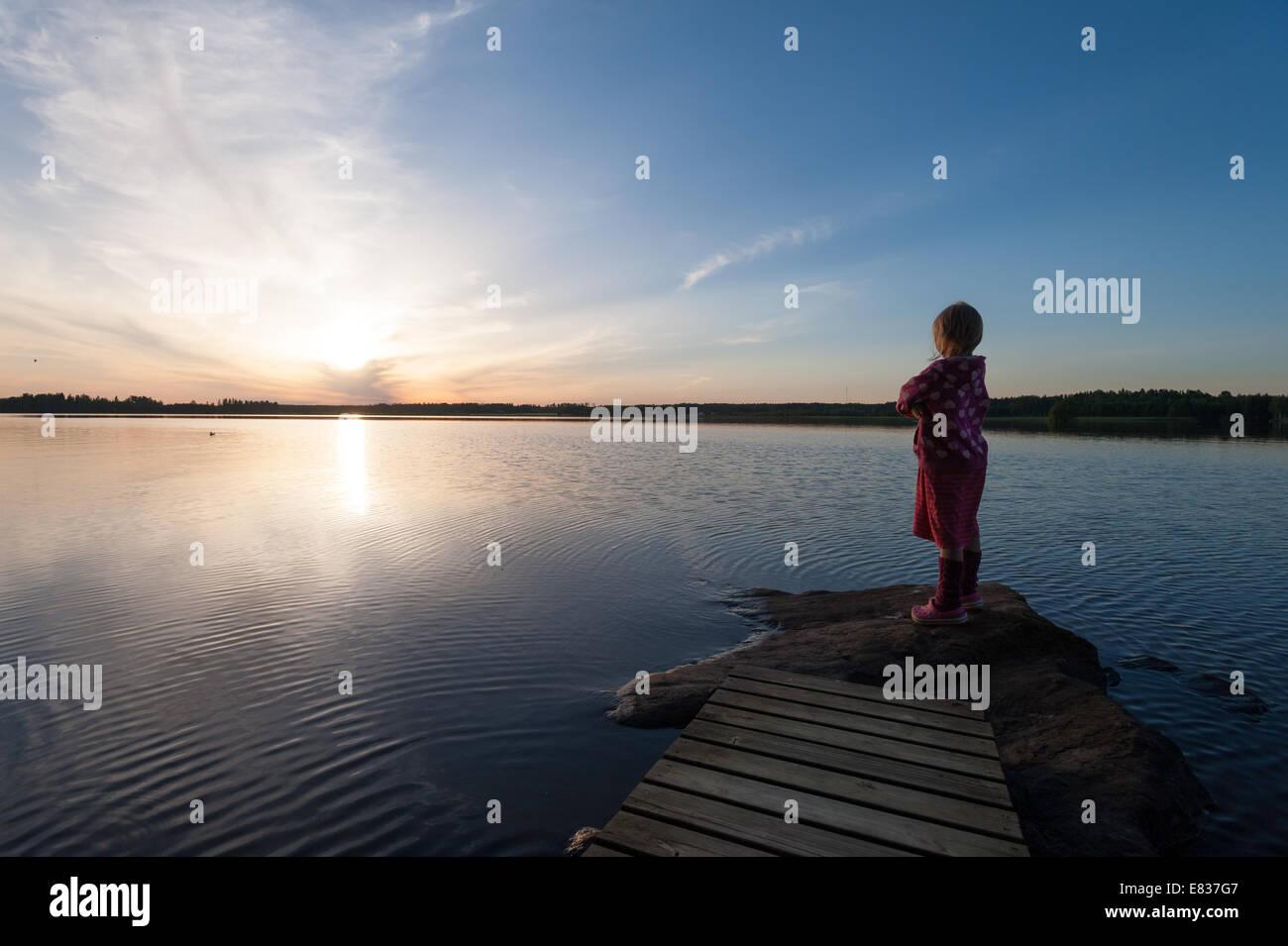 Bambino in piedi dalla riva del lago tarda serata estiva Foto Stock