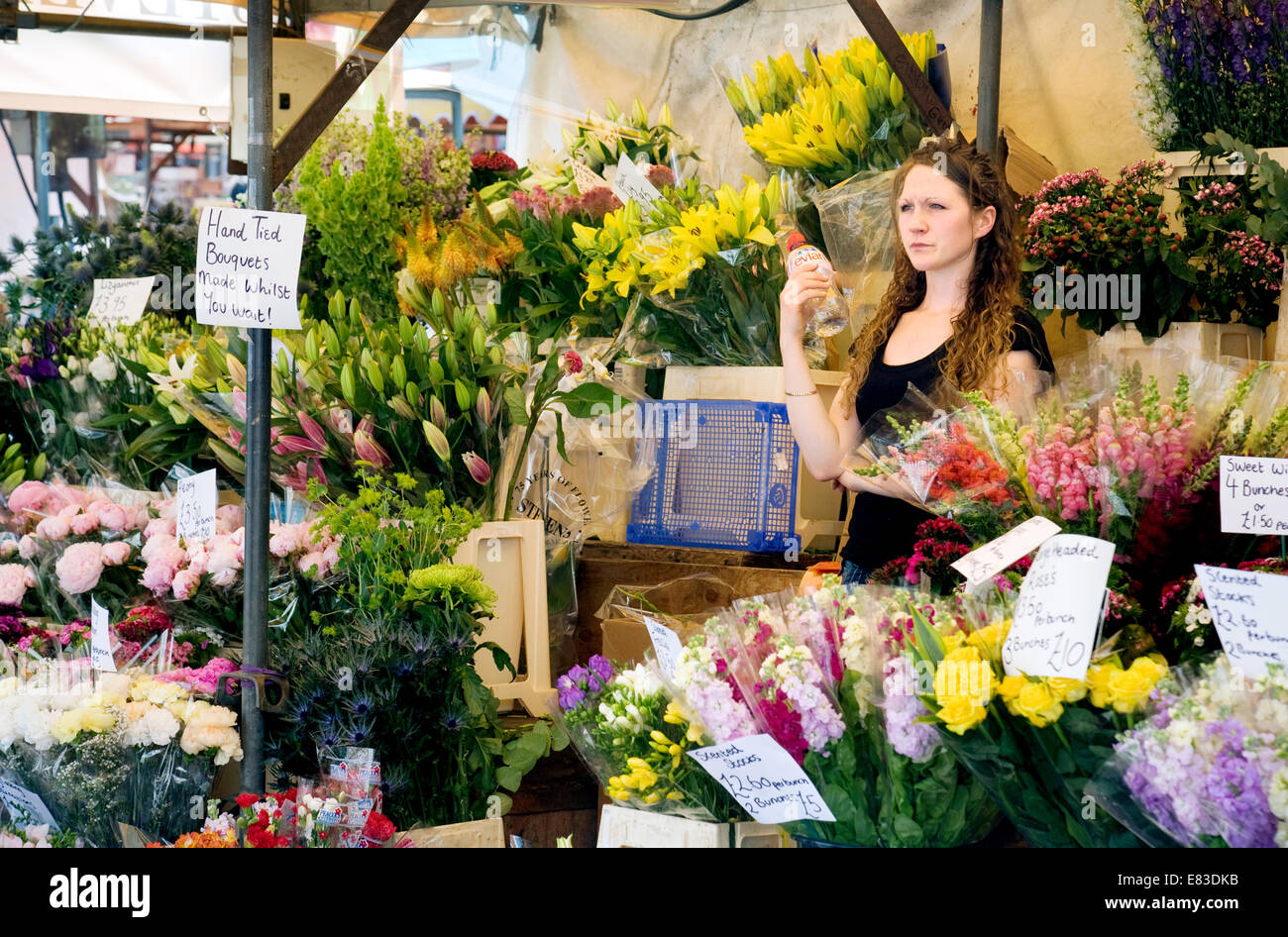 Una fiorista donna nella sua bancarella di fiori che vende fiori al mercato di Cambridge, Cambridge, Inghilterra, Regno Unito Foto Stock