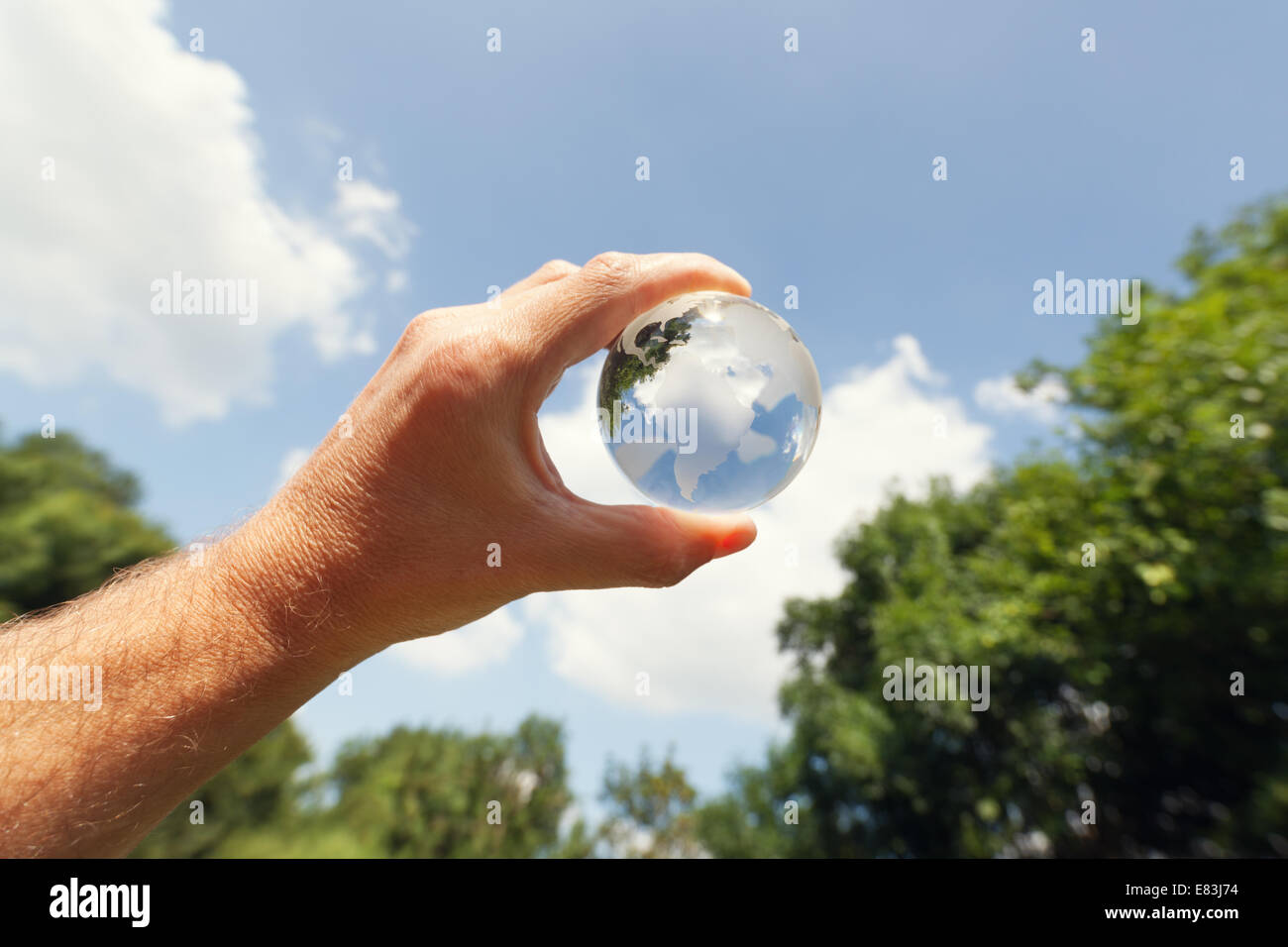 Tenendo un globo di vetro al cielo blu,alberi e il campo Foto Stock