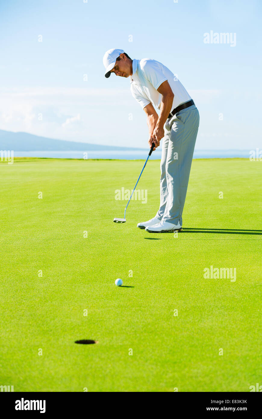 Il Golfer sul putting green di colpire la pallina da golf nel foro Foto Stock
