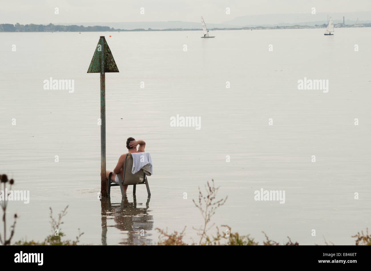 Uomo seduto su una sedia in acqua a prendere il sole in un giorno di nebbia, Langstone Harbour, Hampshire, Inghilterra, Foto Stock