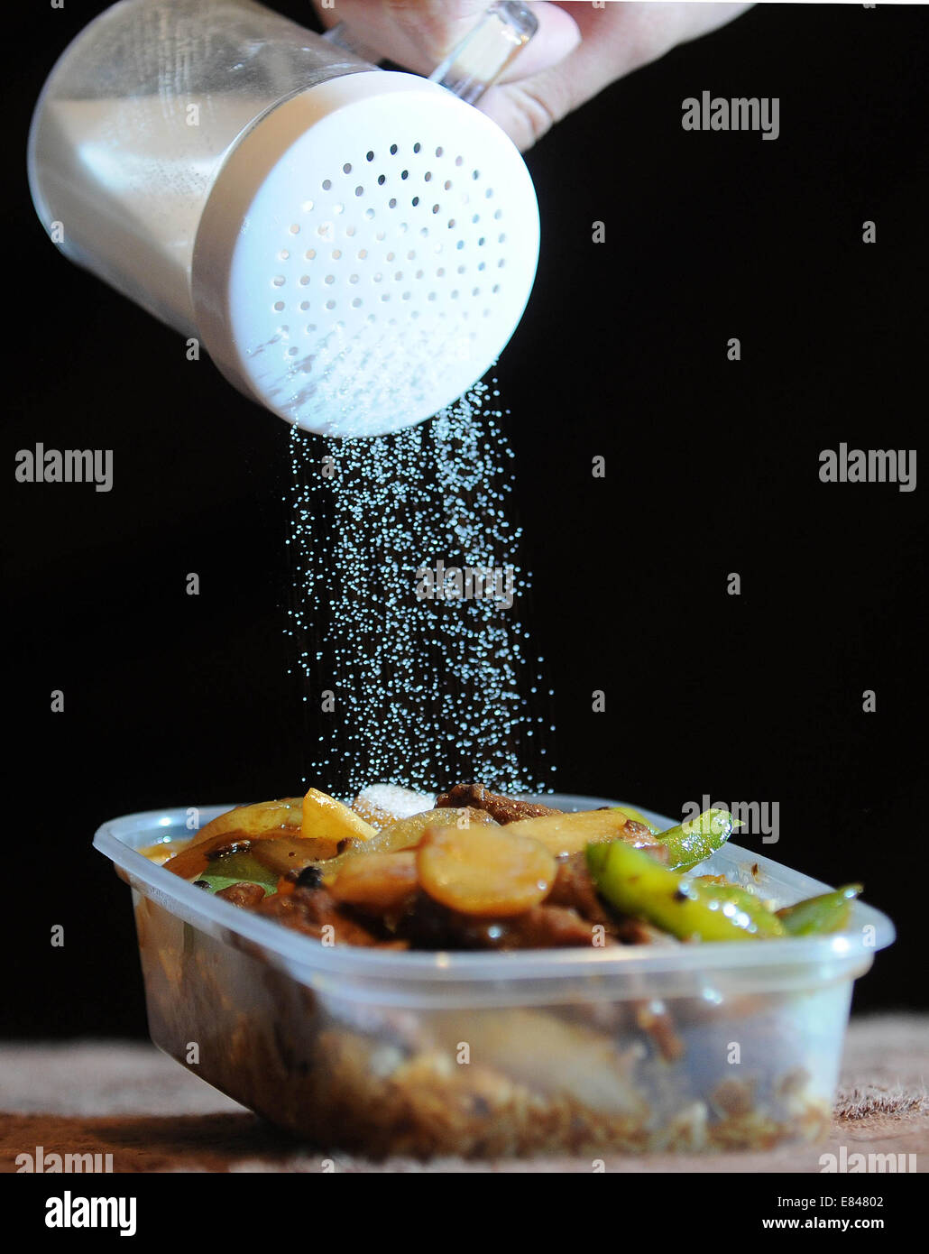 Cibo da asporto con sale che viene versato su dal di sopra. Alti livelli di sale nel cibo spazzatura cause di alta pressione sanguigna e la malattia di cuore Foto Stock