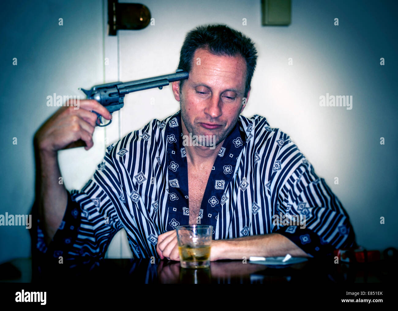 Uomo in accappatoio con la pistola alla testa e un bicchiere di Whiskey Foto Stock