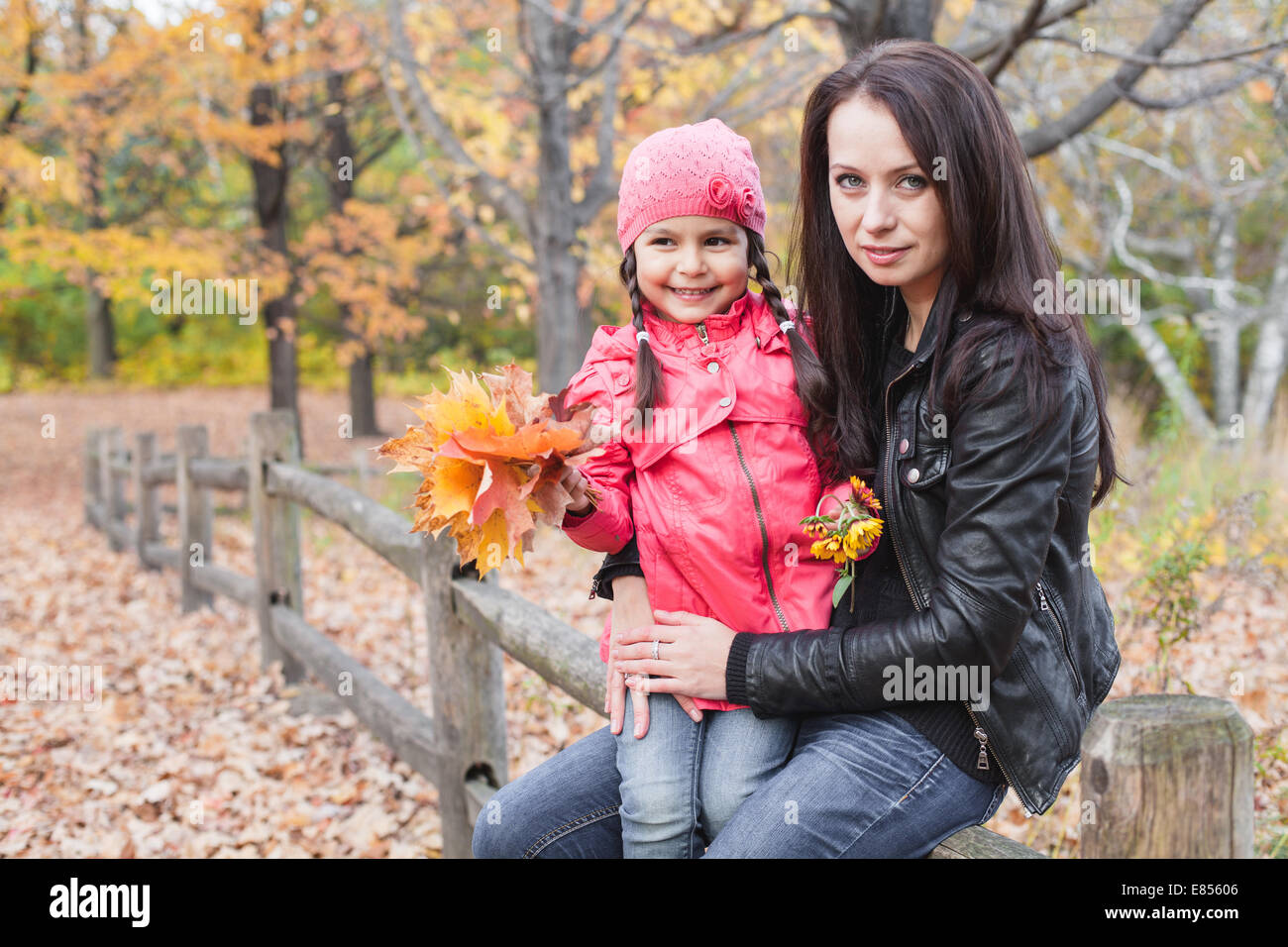 Bambina con la madre tenendo le foglie di autunno in un parco di autunno Foto Stock
