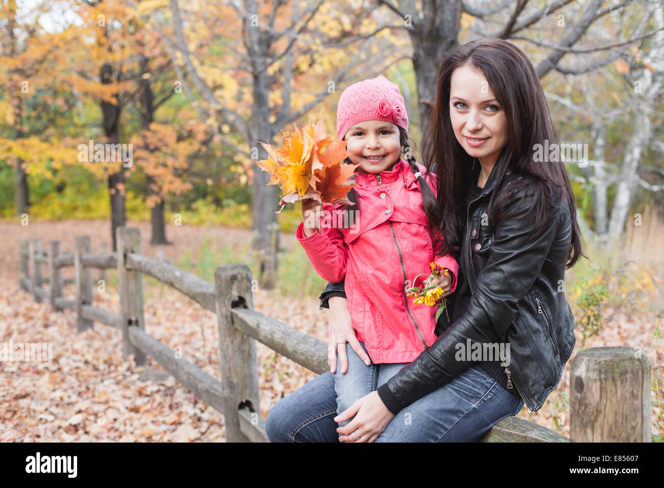 Bambina con la madre tenendo le foglie di autunno in un parco di autunno Foto Stock