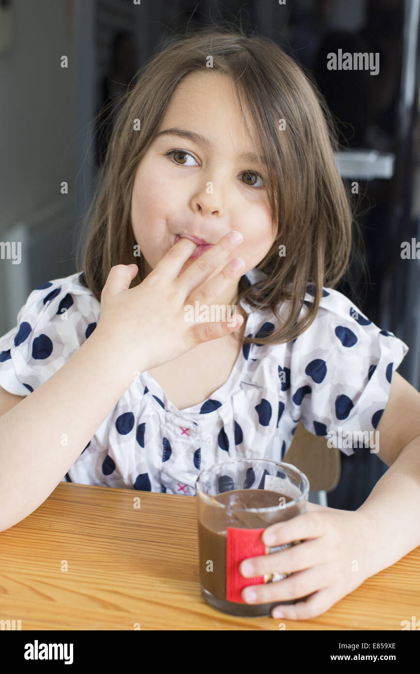 Bambina di mangiare in salsa di cioccolato da un vaso con le dita Foto Stock