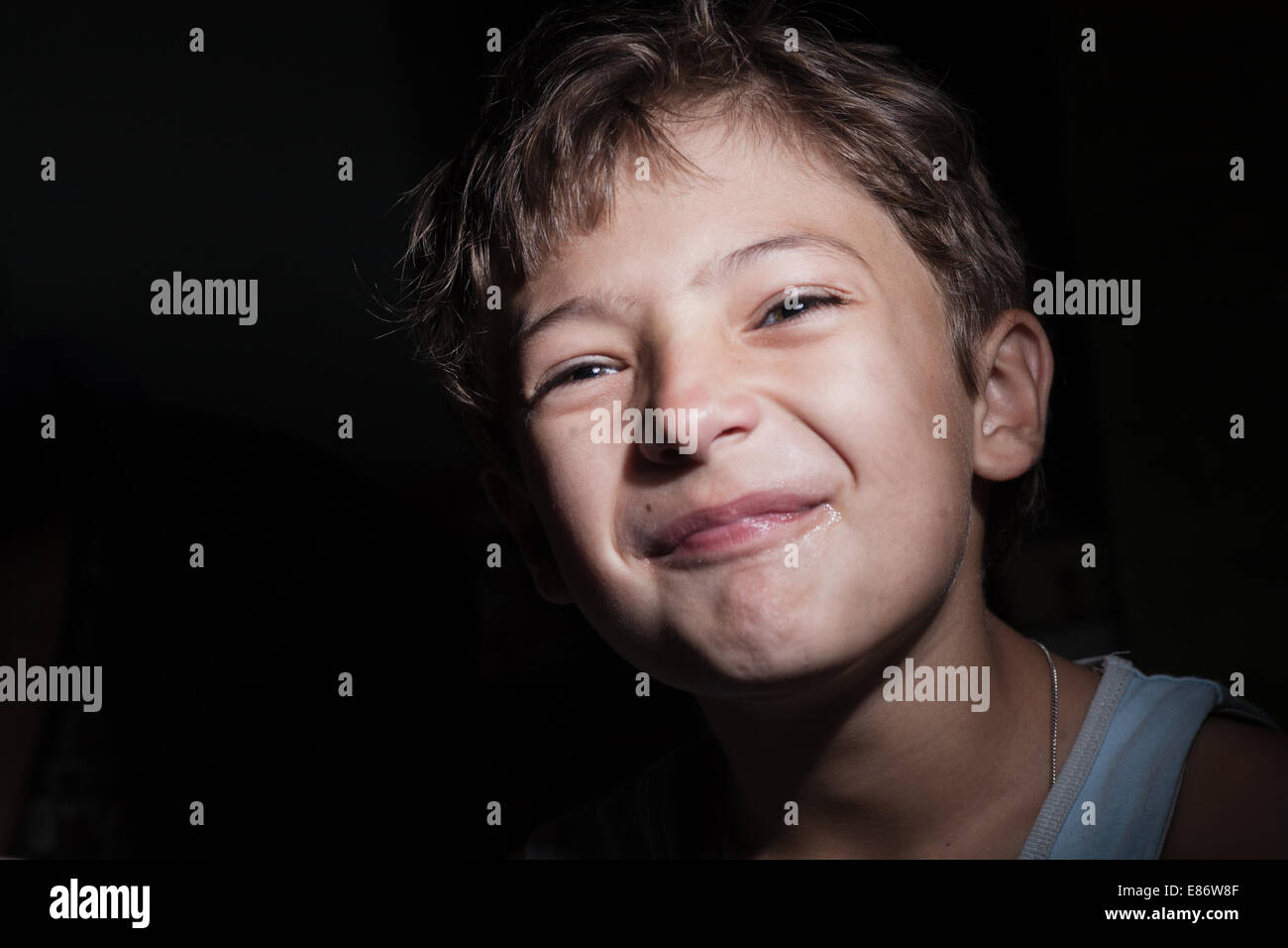 Ragazzo nel buio grido o rendere volti, luce focalizzata sulla faccia, sfondo al buio Foto Stock