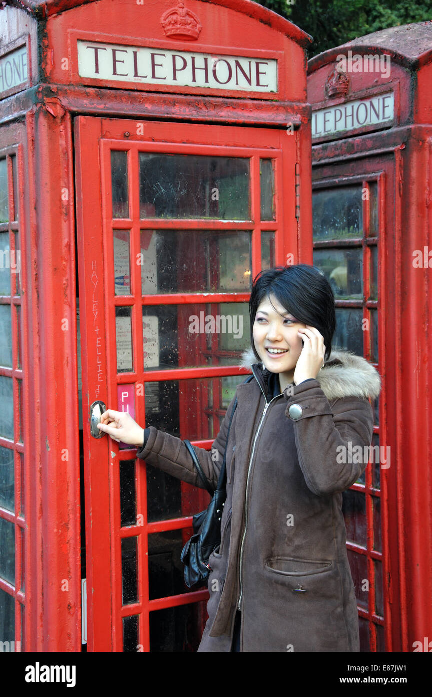 Giovane donna giapponese utilizzando il telefono cellulare al di fuori di un tradizionale telefono rosso scatola, England, Regno Unito Foto Stock