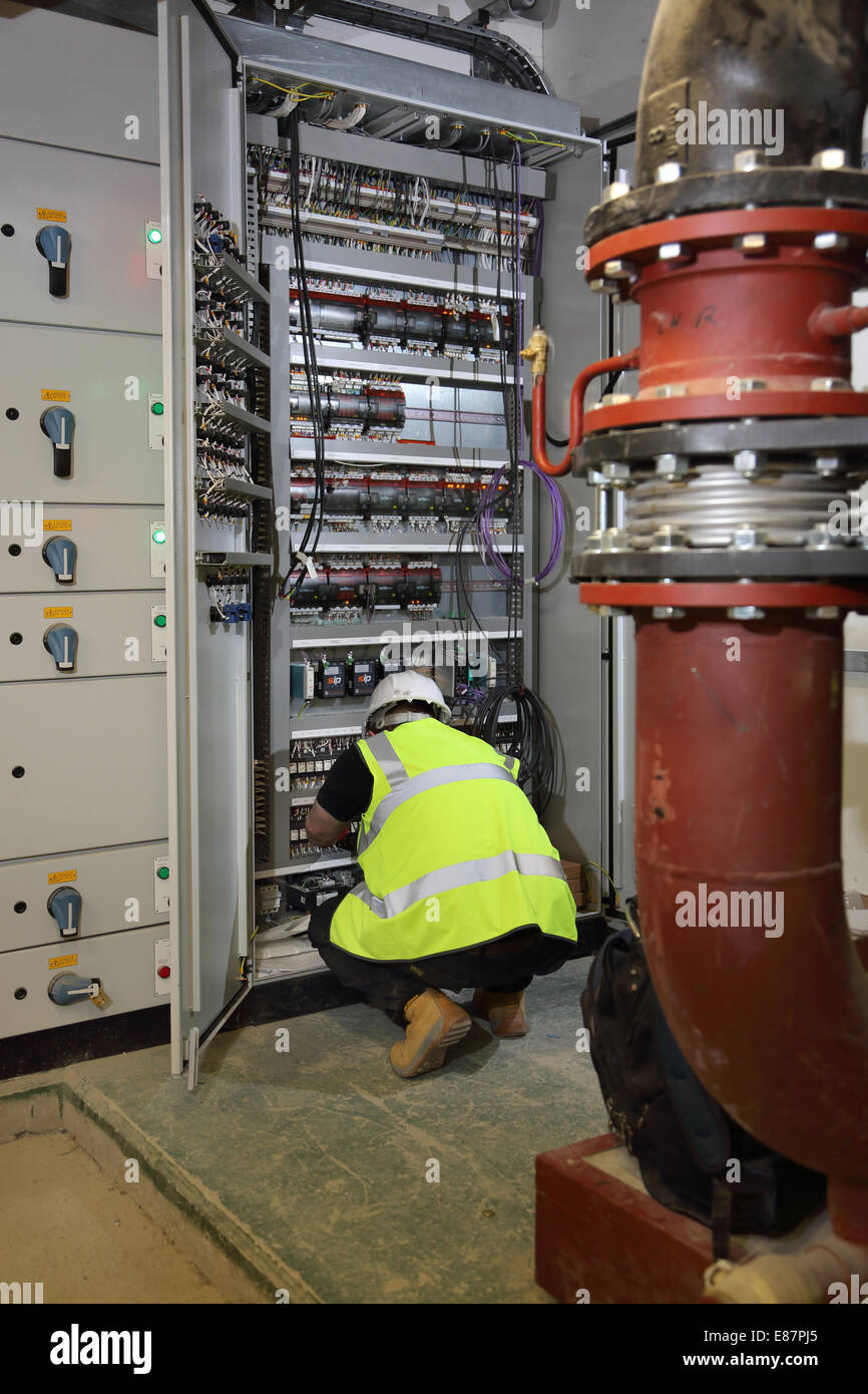 Un edificio services engineer lavora in un armadio a comando elettrico nel seminterrato sala impianto di un grande blocco di ufficio Foto Stock