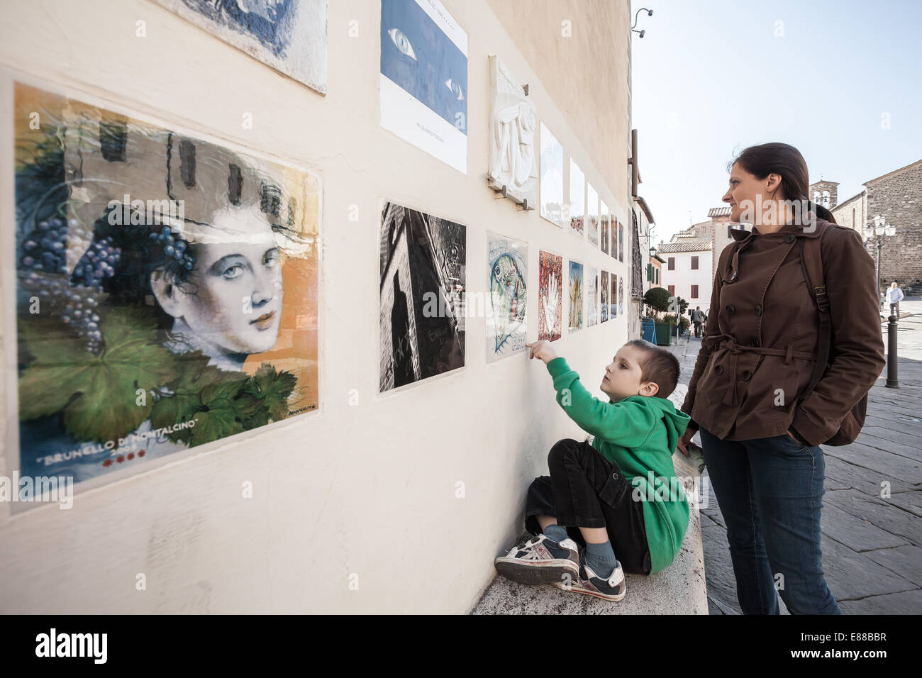 Kid e la sua mamma guardando spot mostra le foto per il Brunello di Montalcino visualizzati sul muro della Strada italiano Foto Stock