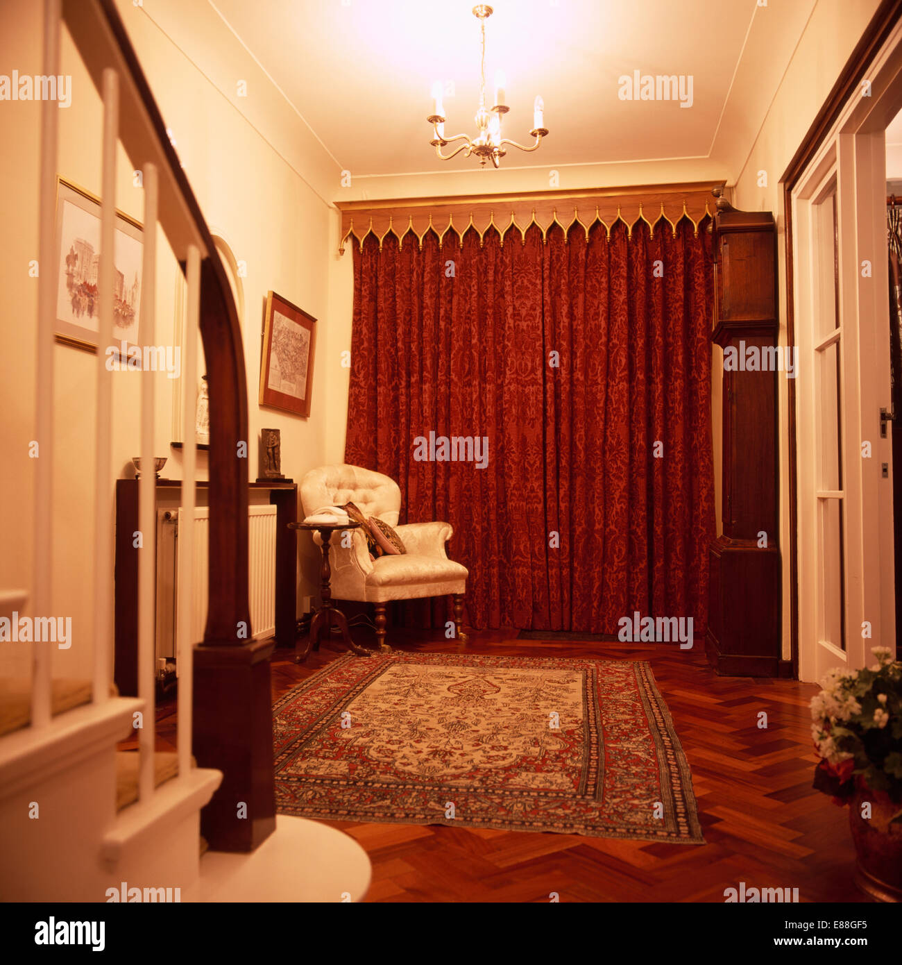In legno in stile gotico mantovane sopra tende rosse nella sala tradizionale con poltrona e grande tappeto sul pavimento in parquet Foto Stock