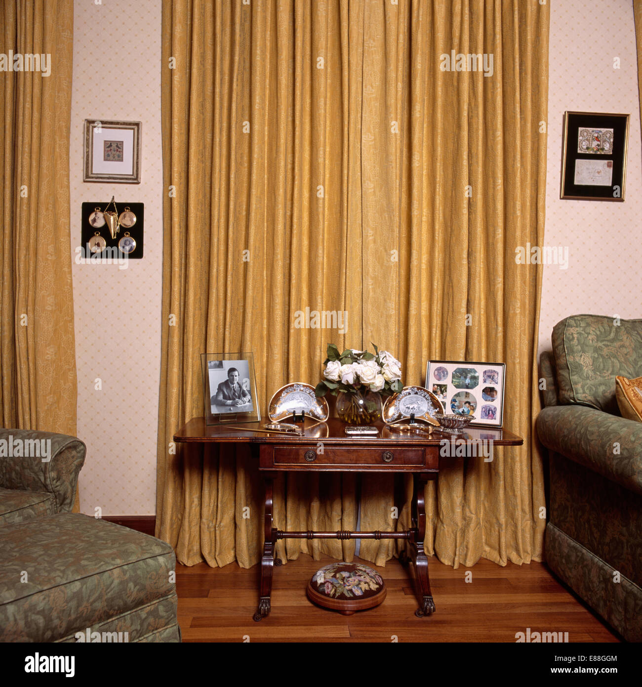 Fotografie incorniciate sul piccolo tavolo di fronte tende di color ocra in salotto Foto Stock