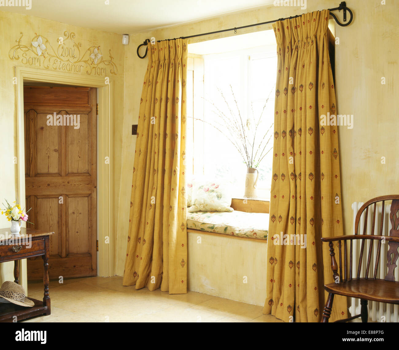Antique Windsor sedia accanto alla finestra con il cuscino sulla finestra-sede e modellato tende gialle nel paese hall Foto Stock