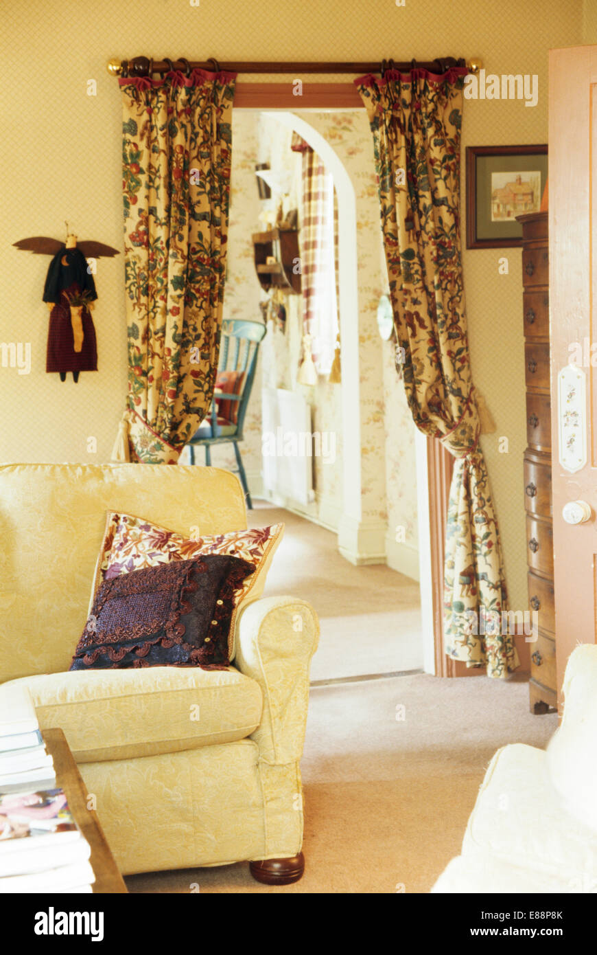 La crema divano in cottage soggiorno con tende a motivi geometrici sulla porta di ingresso alla sala piccola Foto Stock