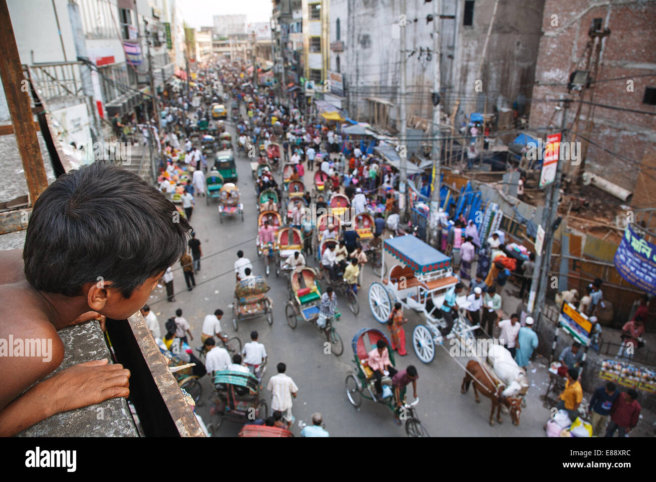 Un ragazzo orologi il traffico stradale con rickshaws sulla strada principale nella vecchia città di Dacca in Bangladesh Foto Stock