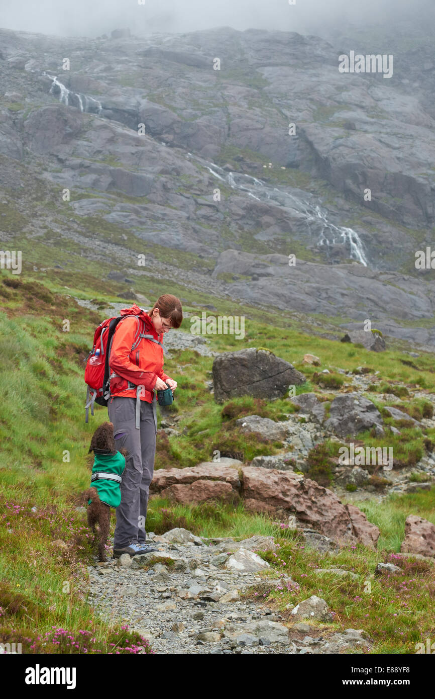 Un escursionista alimentando il loro cane tratta mentre fuori su una passeggiata in montagna sull'Isola di Skye. Foto Stock