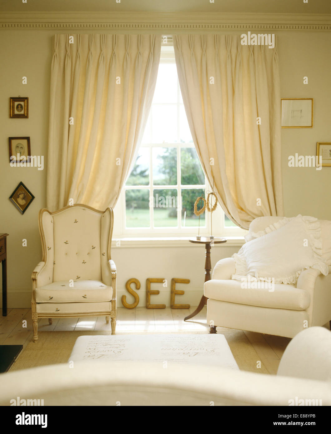 Poltrone su entrambi i lati della finestra con la crema tende in country living room con oro lettere di legno sul pavimento Foto Stock