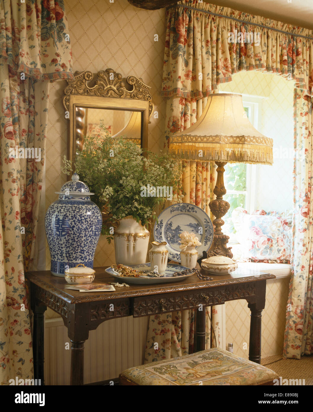 Lampada accesa e alte blu vaso cinese sul tavolo antico in cottage camera da letto con tende dai motivi floreali Foto Stock