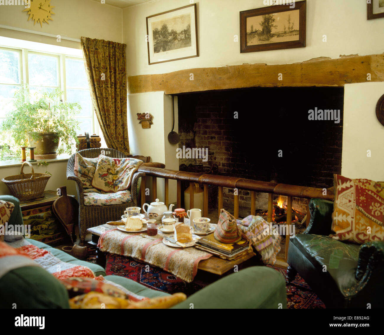 Tavolino set per il tè davanti al fuoco nel cottage accogliente soggiorno con comodo divano e poltrona Foto Stock