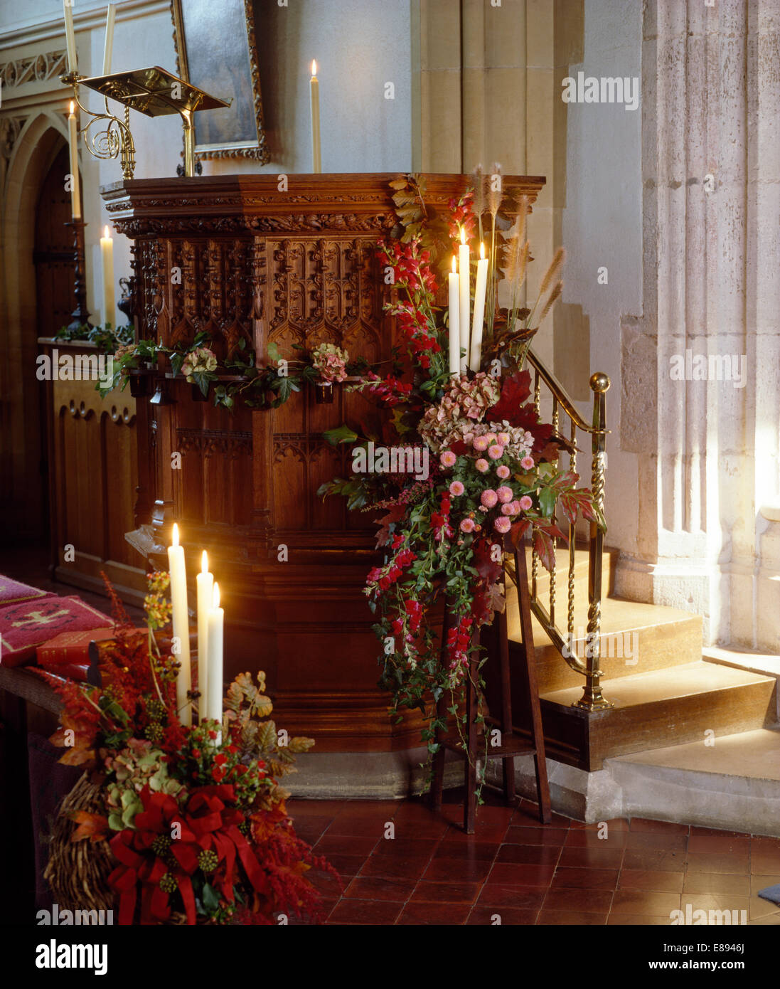 Le rose rosa e bacche rosse in colorate composizioni floreali accanto a pulpito in chiesa decorata per un matrimonio estivo Foto Stock