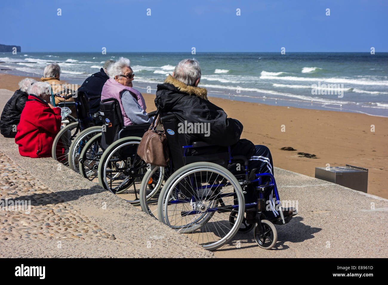 Gruppo di anziani in carrozzina sulla spiaggia guardando l'acqua in un freddo giorno lungo la costa del Mare del Nord Foto Stock