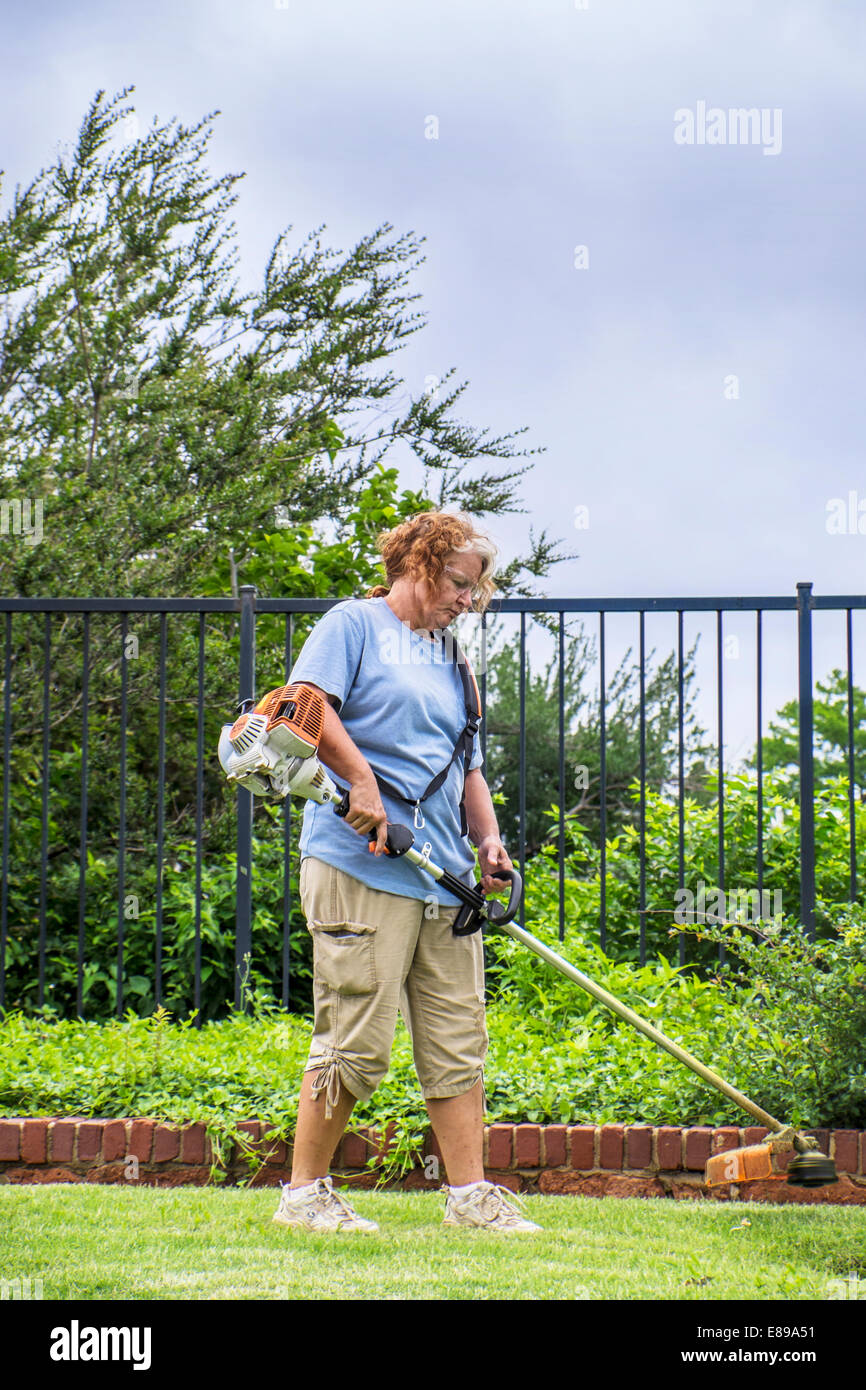 Un Caucasian parco cittadino lavoratore di sesso femminile nel suo 50s utilizza un rifinitore di erbaccia in una città di Oklahoma, Oklahoma parco pubblico. Foto Stock