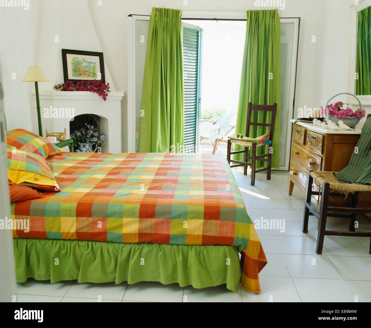 Colorato multi-colore di lenzuola sul letto in bianco camera da letto costiera con verde tende alle finestre Francesi Foto Stock