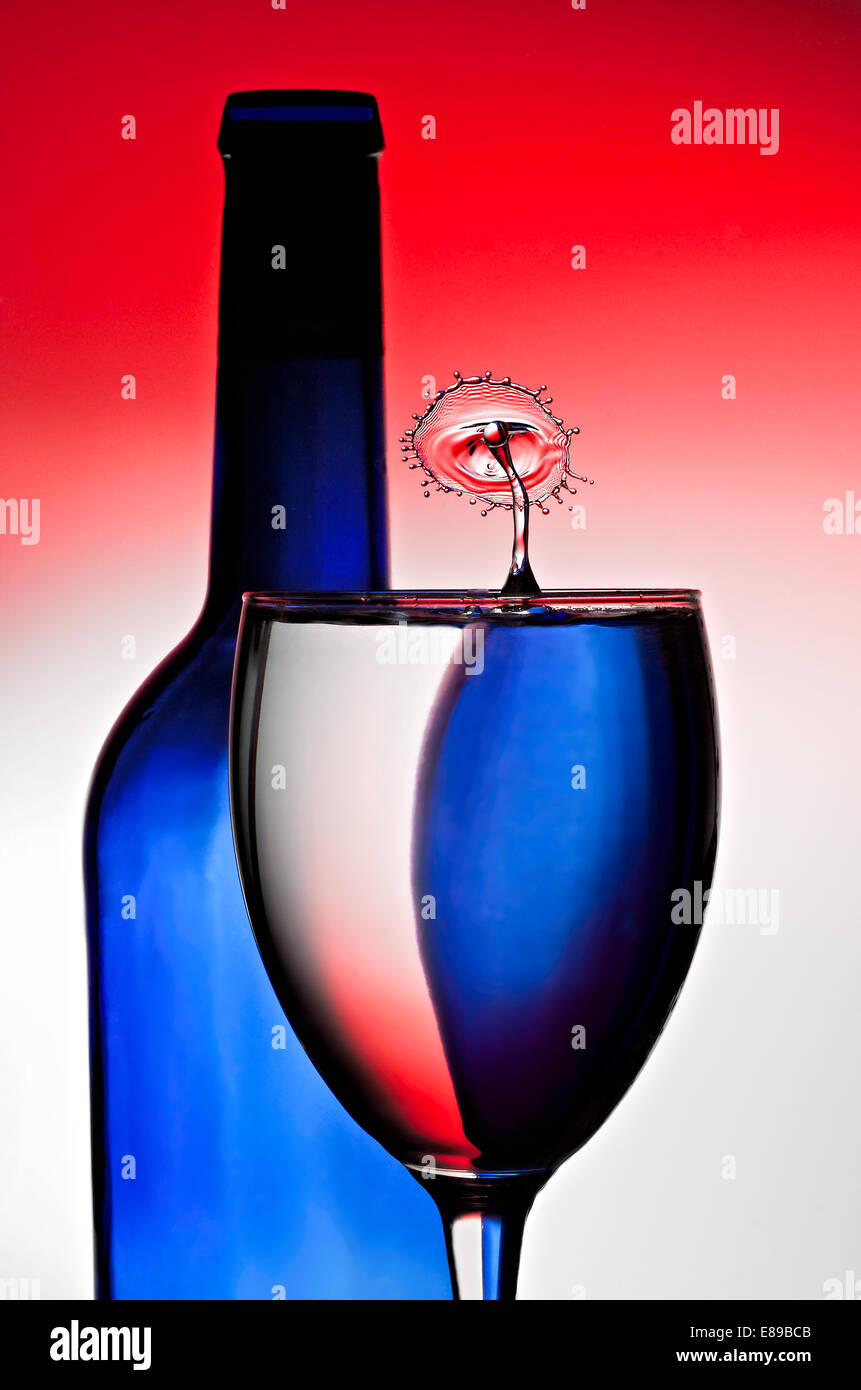 Rosso, bianco e blu sono riflessa e rifratta attraverso la bottiglia di vino e vetro, mentre acqua a una collisione si verifica sulla superficie. Foto Stock