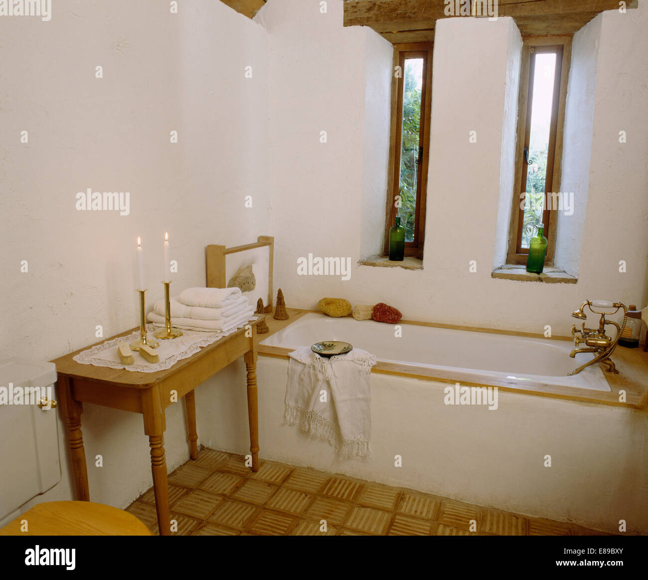 Strette finestre sopra il bagno in fienile bagno di conversione con le candele accese sul piccolo tavolo di pino Foto Stock