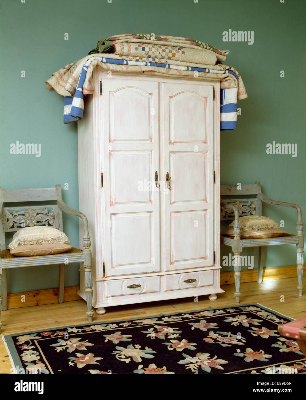 Ripiegate patchwork trapunte su bianco armadio dipinto in colore verde pallido camera da letto con tappeto floreale e di colore grigio pallido sedie Foto Stock