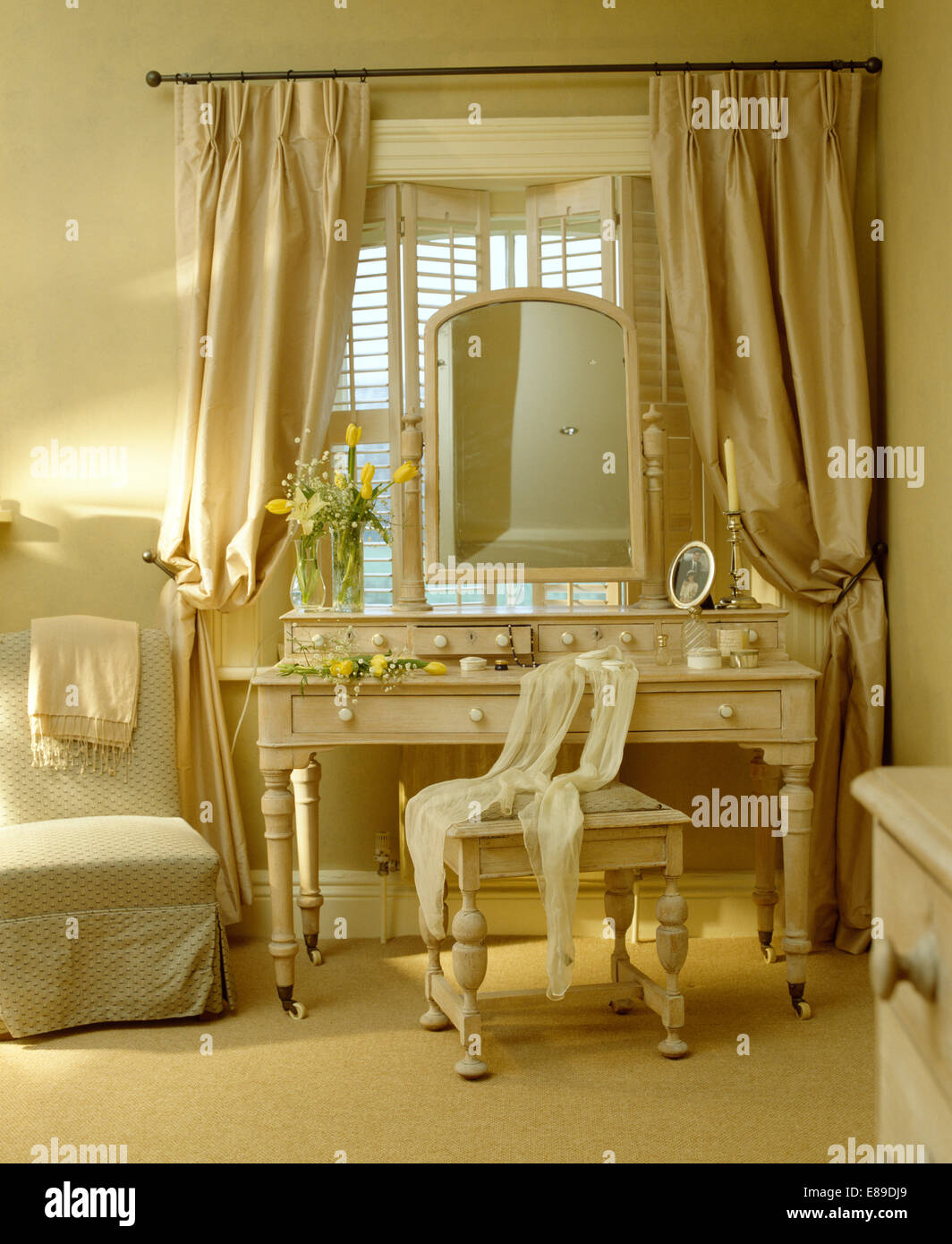 Crema di pesanti tende di seta sulla finestra con persiane in stile piantagione al di sopra dello specchio e dipinte di color crema toeletta Foto Stock