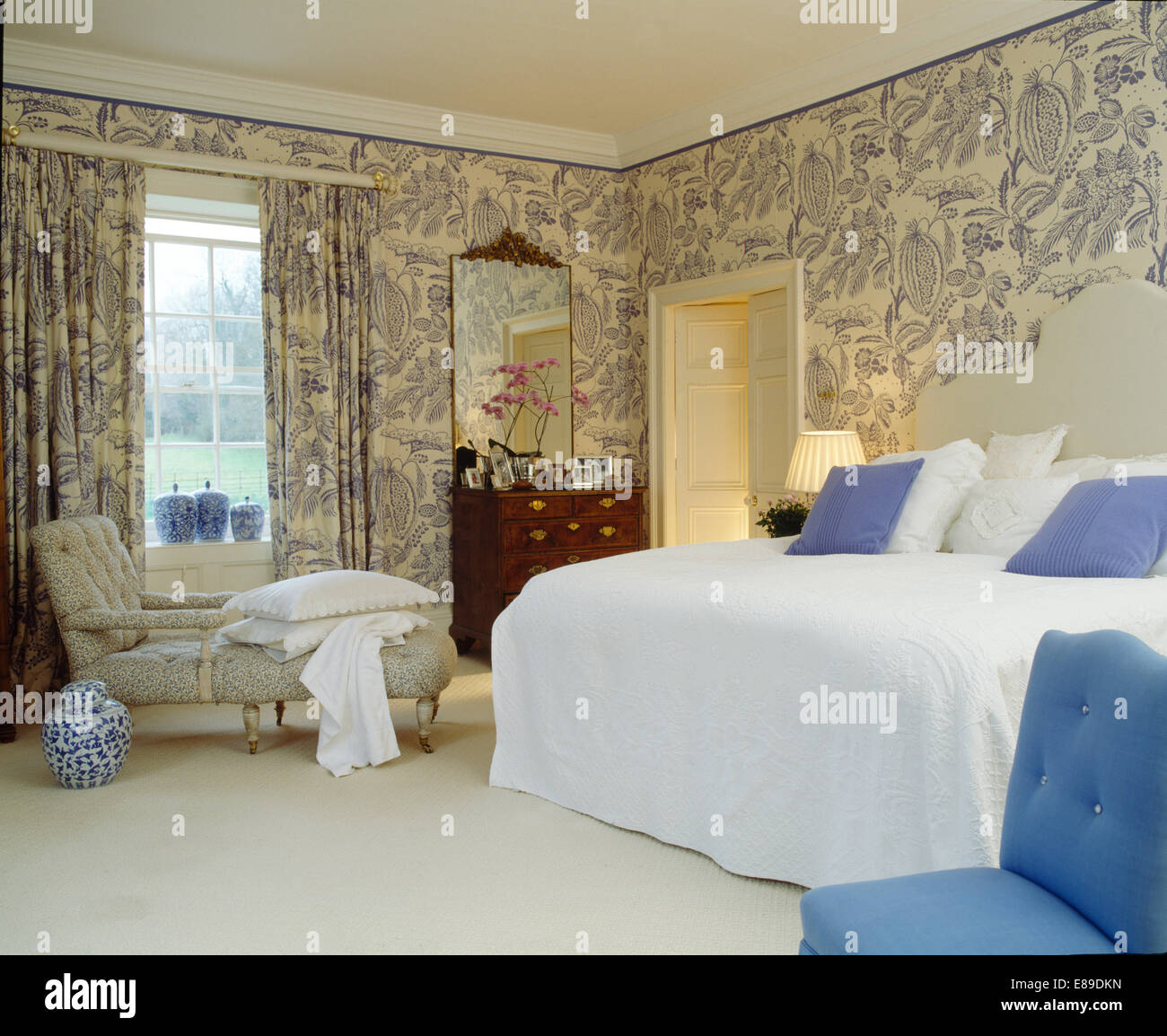 Blue+sfondo bianco e tende coordinate nel paese camera da letto con chaise longue e letto con trapunta bianca Foto Stock