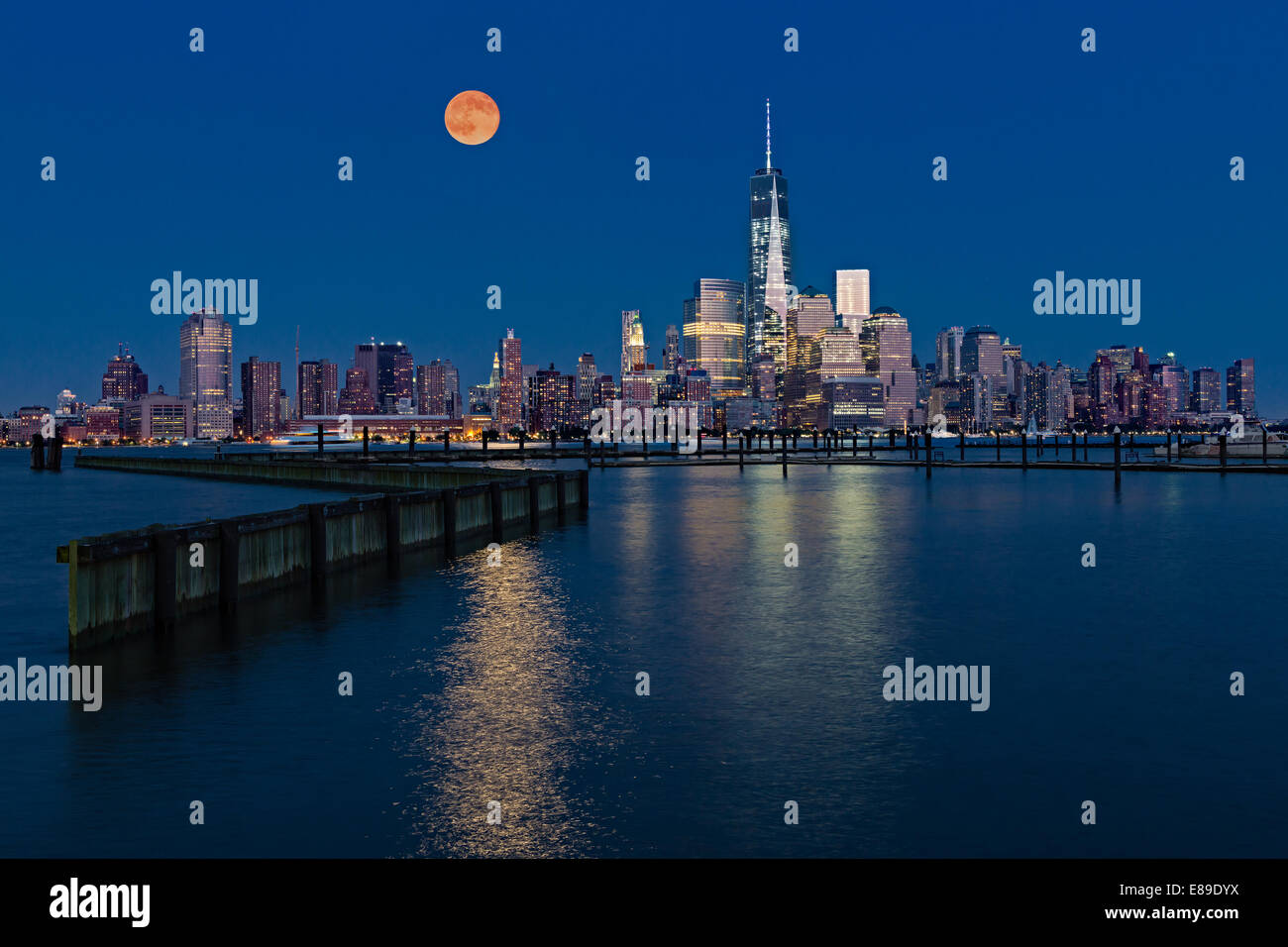 La super luna sorge oltre i grattacieli illuminati nella parte inferiore dello skyline di Manhattan lungo One World Trade Center. Foto Stock