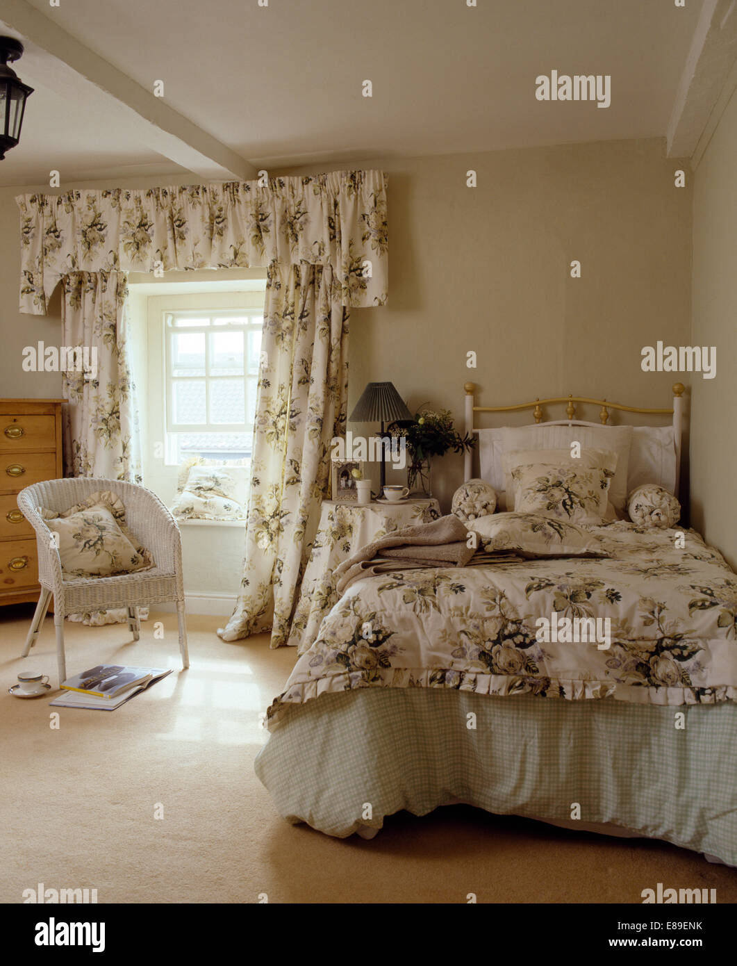 Rose tende a motivi geometrici e trapunta corrispondenti sul letto in bianco cottage camera da letto con Lloyd Loom sedia Foto Stock
