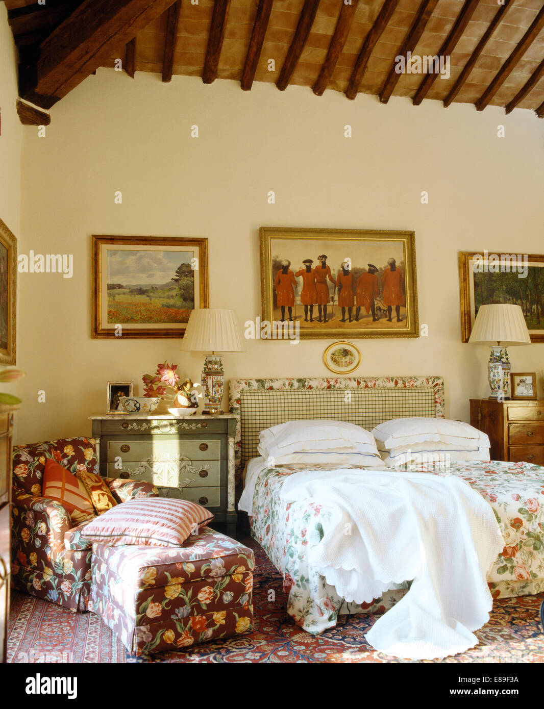 Le immagini sulla parete sopra il letto con trapunta floreali e bianco buttare in camera da letto floreale con Poltrona e pouf Foto Stock