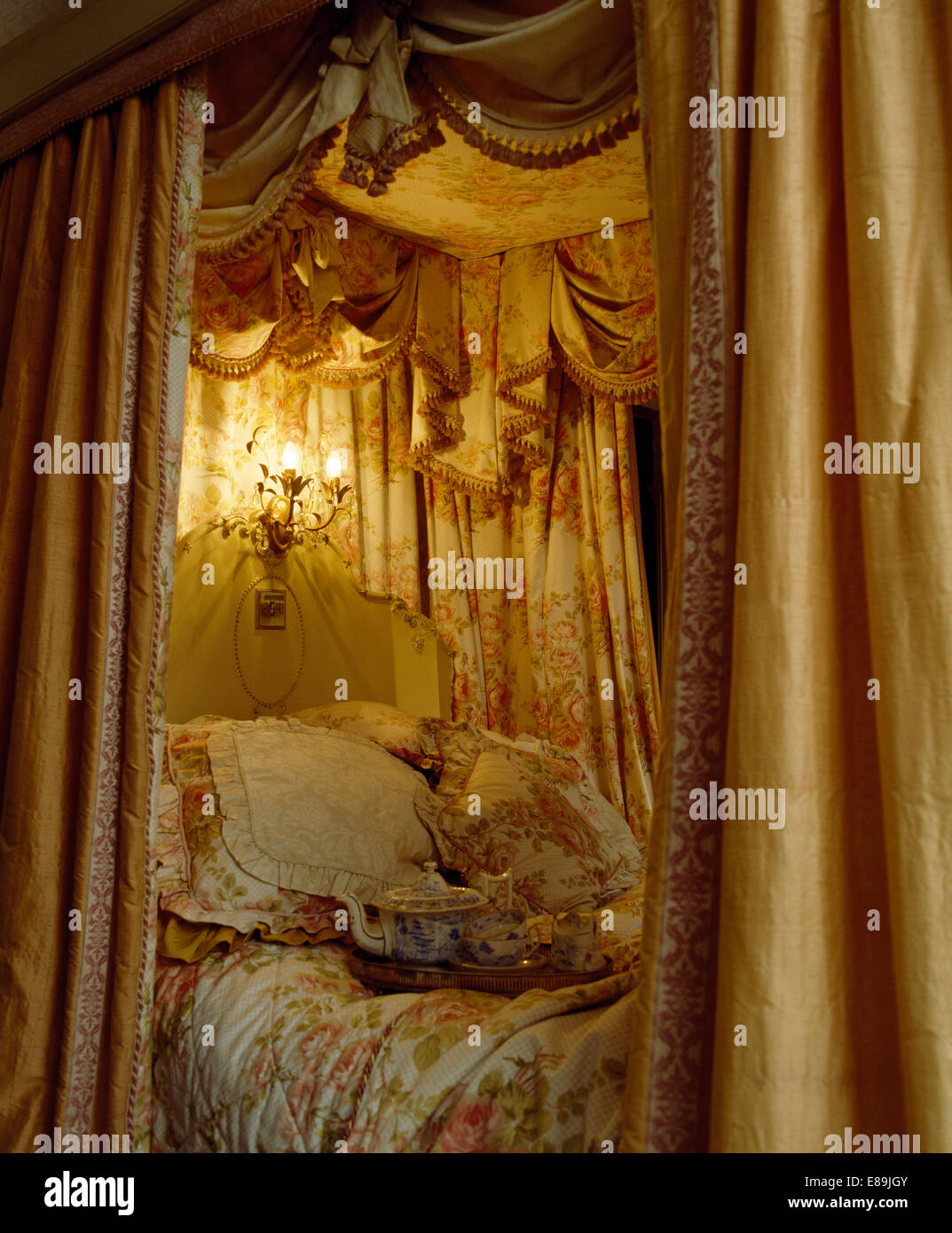Illuminazione fourposter sopra il letto con opulenti tendaggi e biancheria floreale in camera da letto countgry Foto Stock