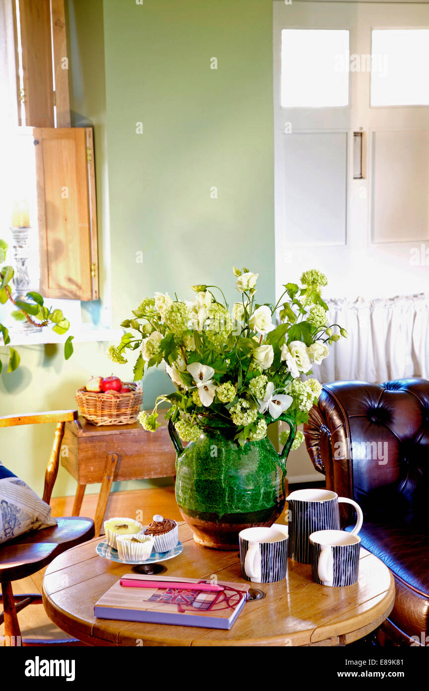 Close-up di fiori color crema in caraffa verde sul tavolo con coppe e torte Foto Stock