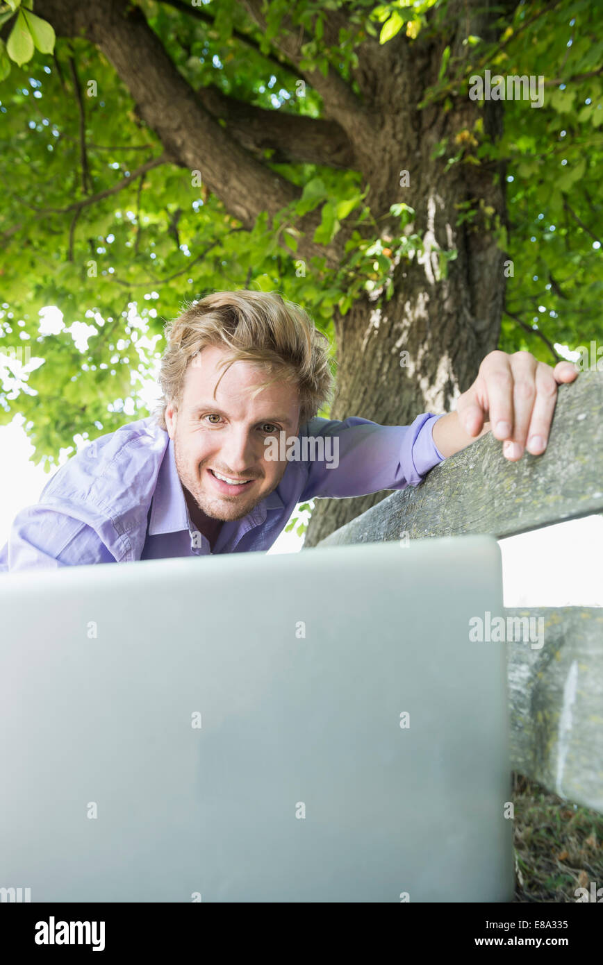 Metà uomo adulto utilizzando laptop su banco, sorridente Foto Stock