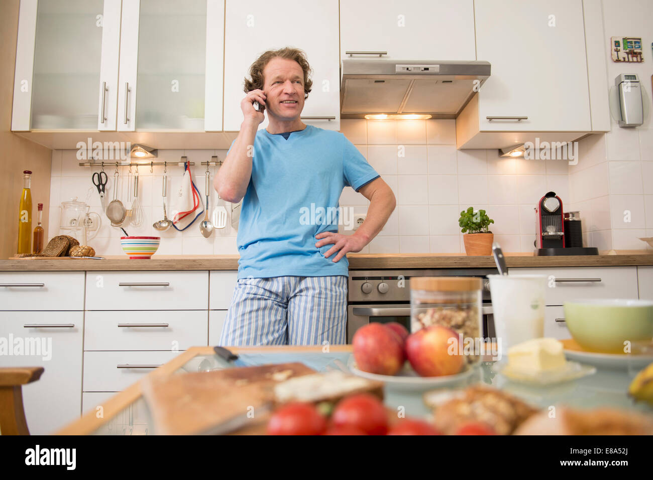 Uomo sorridente sul telefono cellulare in cucina Foto Stock