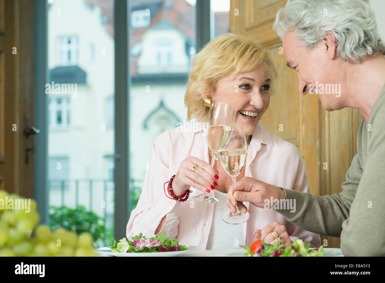 Coppia matura seduta a tavola e il tintinnio di bicchieri di vino spumante, sorridente Foto Stock