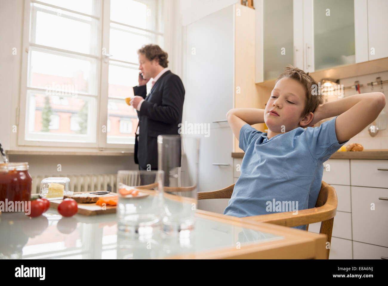 Annoiato ragazzo in cucina con il padre al telefono in background Foto Stock