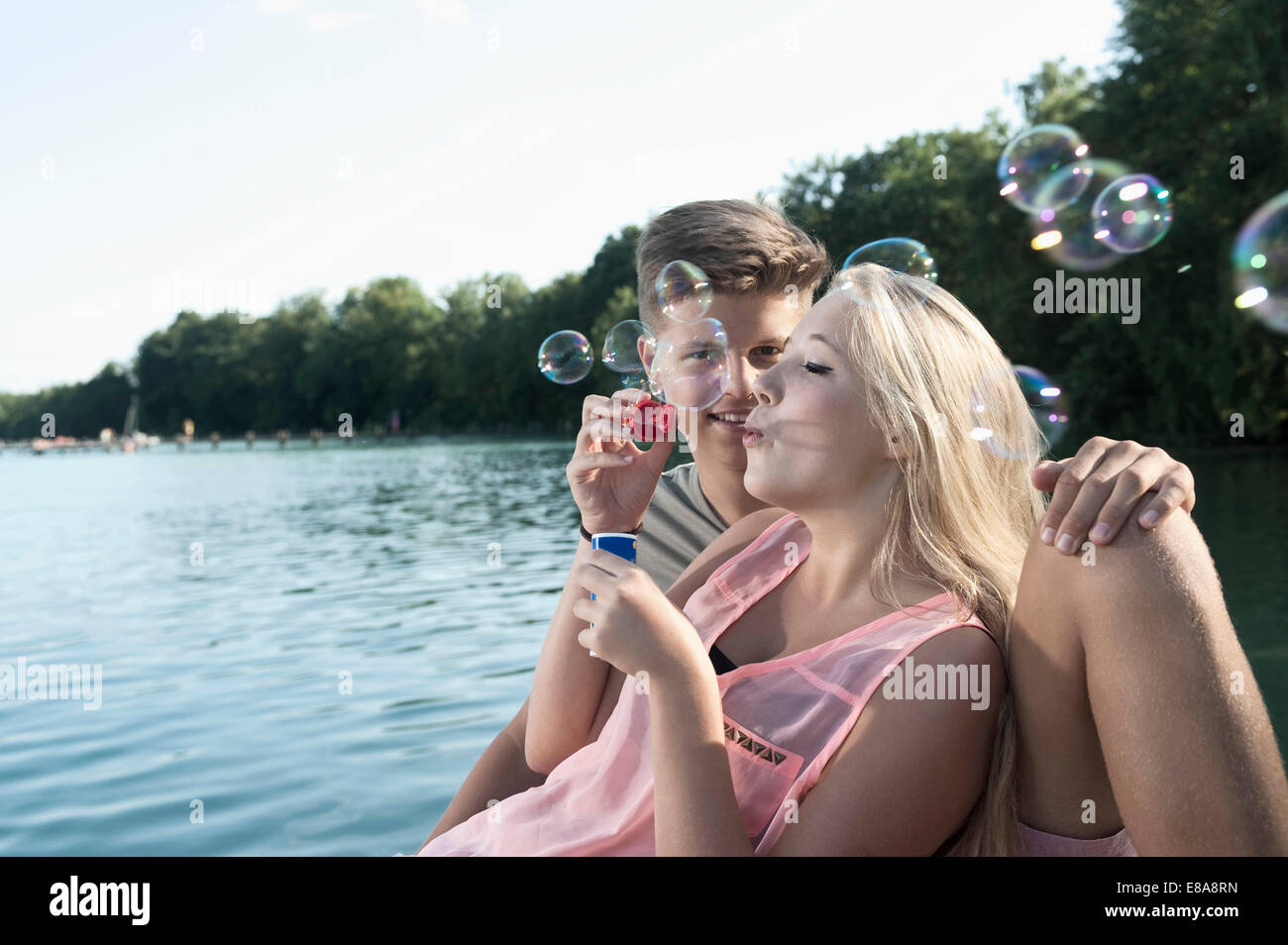 Giovane adolescente soffiando bolle di sapone su un molo al lago Foto Stock