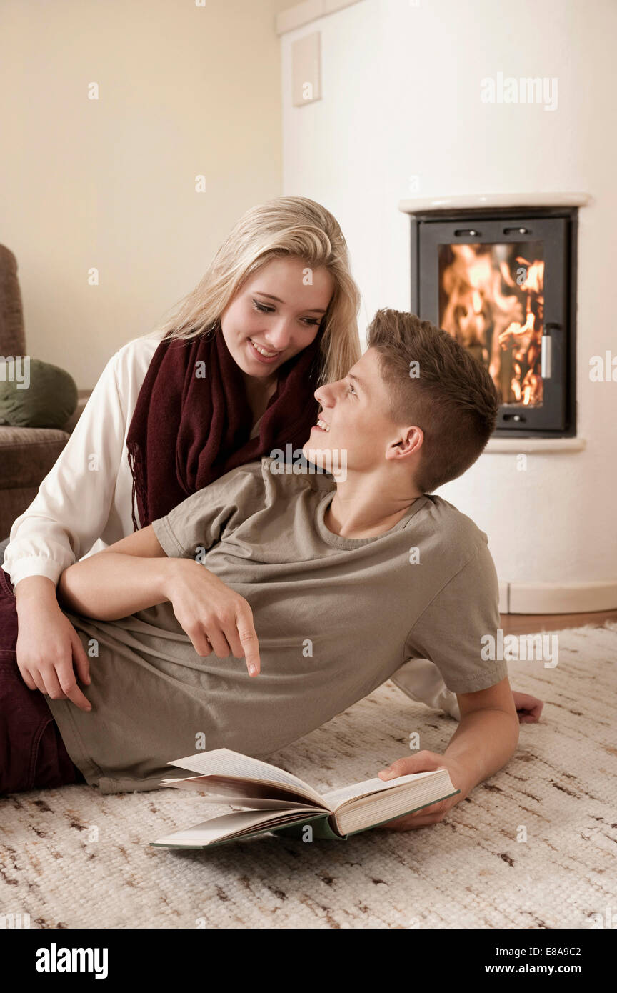 Teenage giovane con libro giacente su un tappeto davanti al caminetto Foto Stock