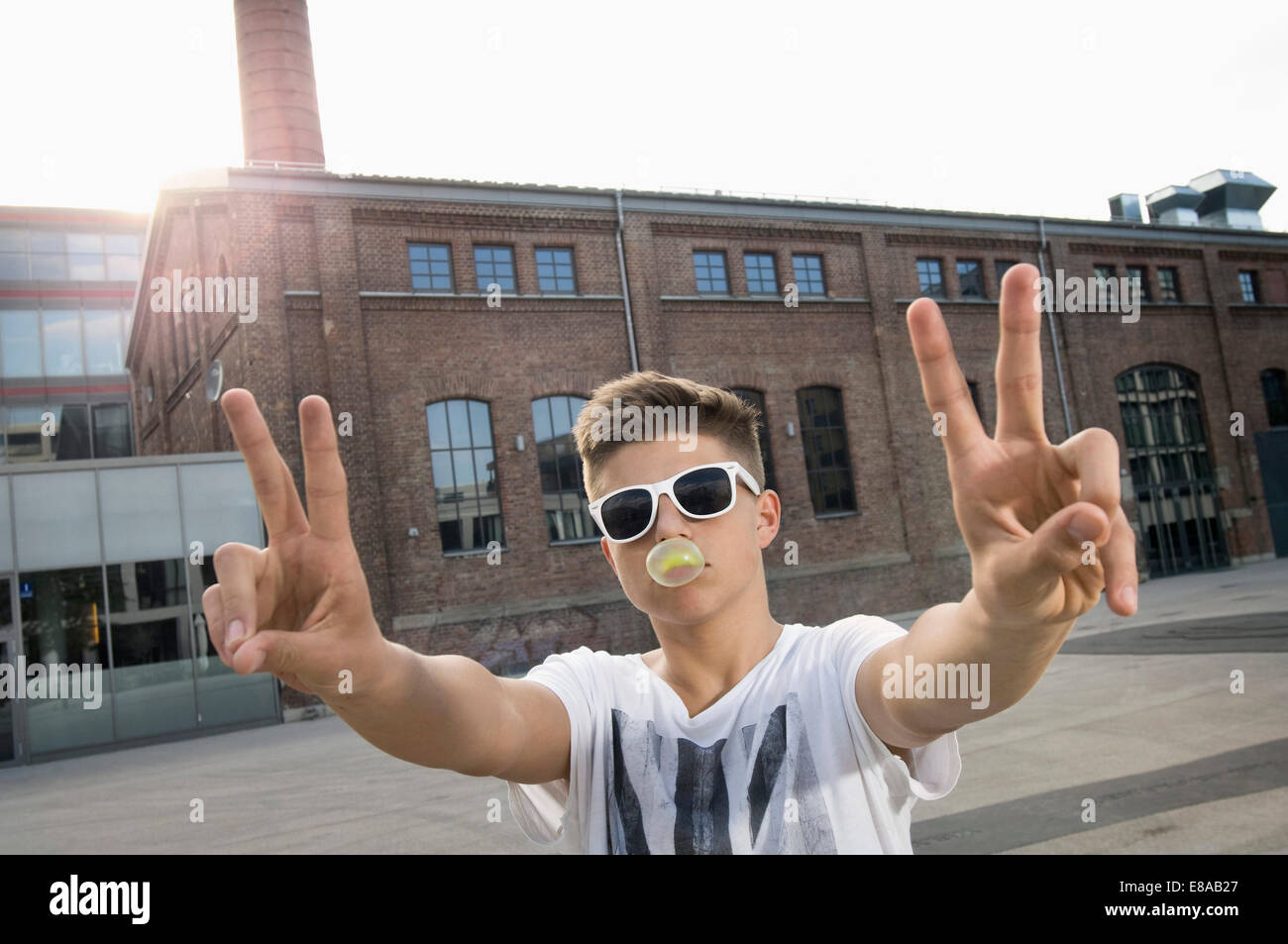 Ragazzo adolescente soffiando bubble gum e che mostra segni di pace Foto Stock