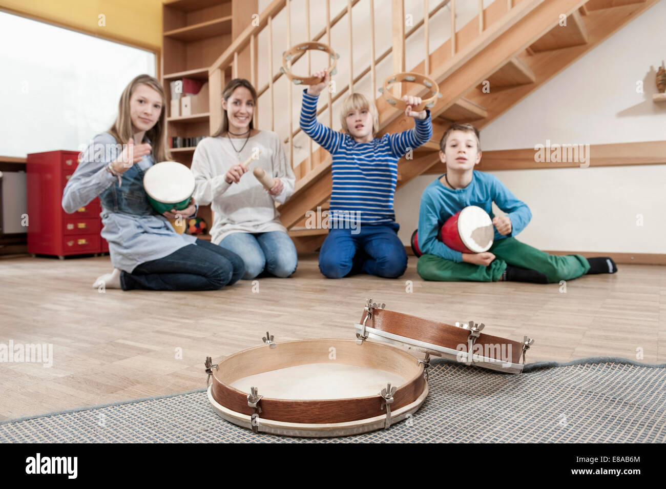 Gruppo di femmina assistente di puericultura e tre bambini drumming Foto Stock